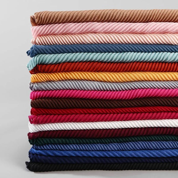 A stack of folded plain cotton full coverage hijab scarves in various shades of pink, blue, red, and brown.