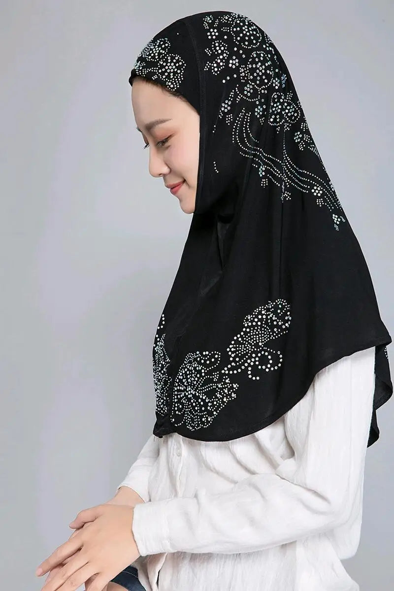 Eine Frau trägt einen eleganten schwarzen Hijab mit weißen Strasssteinen und einem weißen Oberteil.