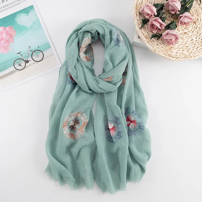 Weiches salbeigrünes, besticktes Wintertuch mit Blumen auf weißem Untergrund.