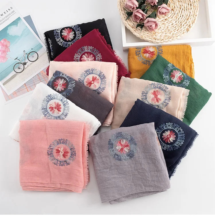 Eine Sammlung von floral bestickten Wintertüchern in verschiedenen Rosa-, Violett-, Grün- und Gelbtönen werden auf einem...