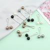A collection of twelve pearl-colored brooch headscarf pins in various shades of gold, silver, and black on a light green back