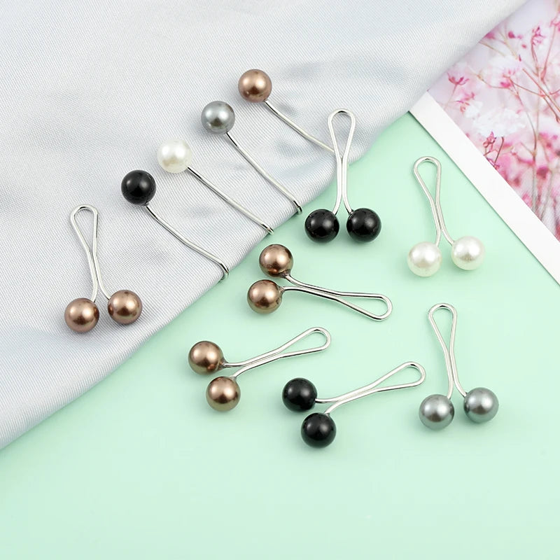 A collection of twelve pearl-colored brooch headscarf pins in various shades of gold, silver, and black on a light green back