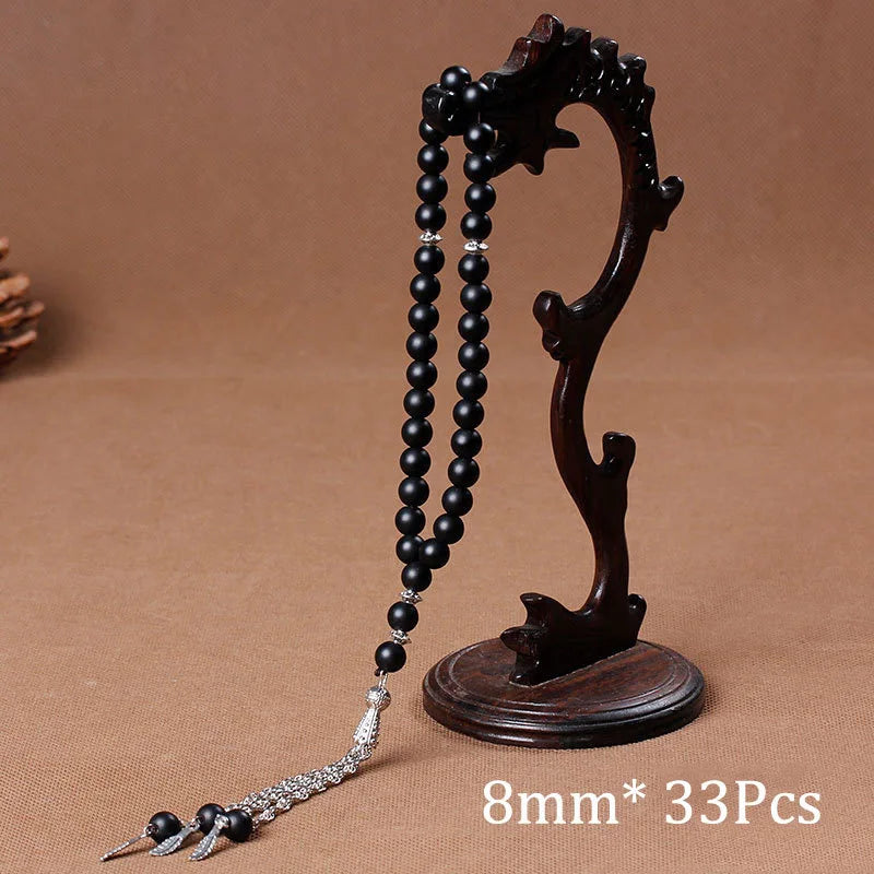 A dark brown wooden prayer bead necklace with black beads and a tassel, displayed on a neutral background.