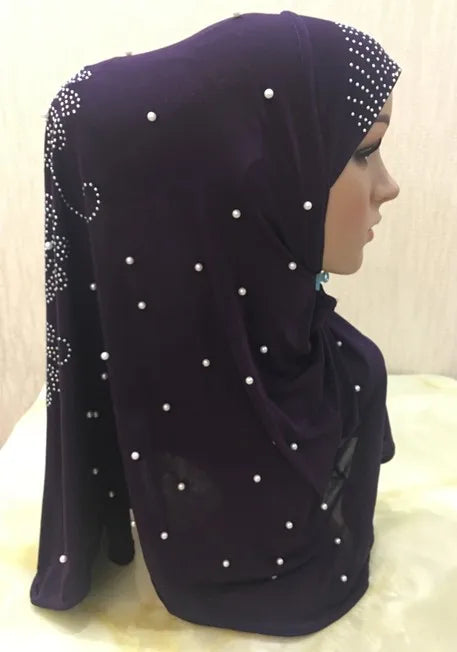 Un pañuelo de hijab de cuentas morado oscuro drapeado sobre la cabeza y el hombro de una modelo.
