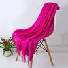 Un chal de cachemira magenta vibrante drapeado sobre una silla blanca, con una planta verde de fondo.