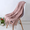Una bufanda de cachemira color rosa empolvado suave drapeada sobre una silla blanca, con detalles de flecos.