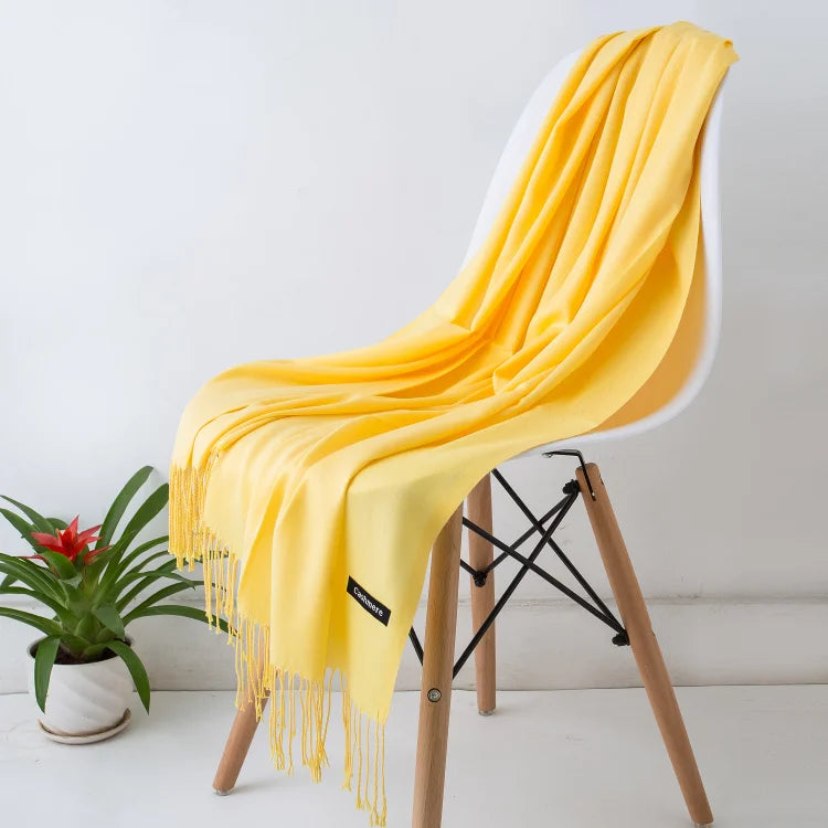 Un chal de cachemira amarillo brillante colgado sobre una silla blanca con patas de madera.