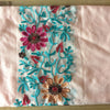 Nahaufnahme eines rosa Stoffes mit aufwendiger floraler Stickerei in Türkis-, Rosa- und Rosttönen.