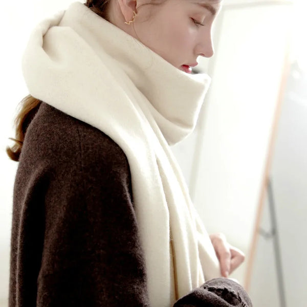 A woman wearing a thick cream wool shawl over a brown coat, looking down.