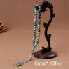 A dark wooden prayer bead necklace featuring green and purple agate beads and a tassel, displayed on a brown background.
