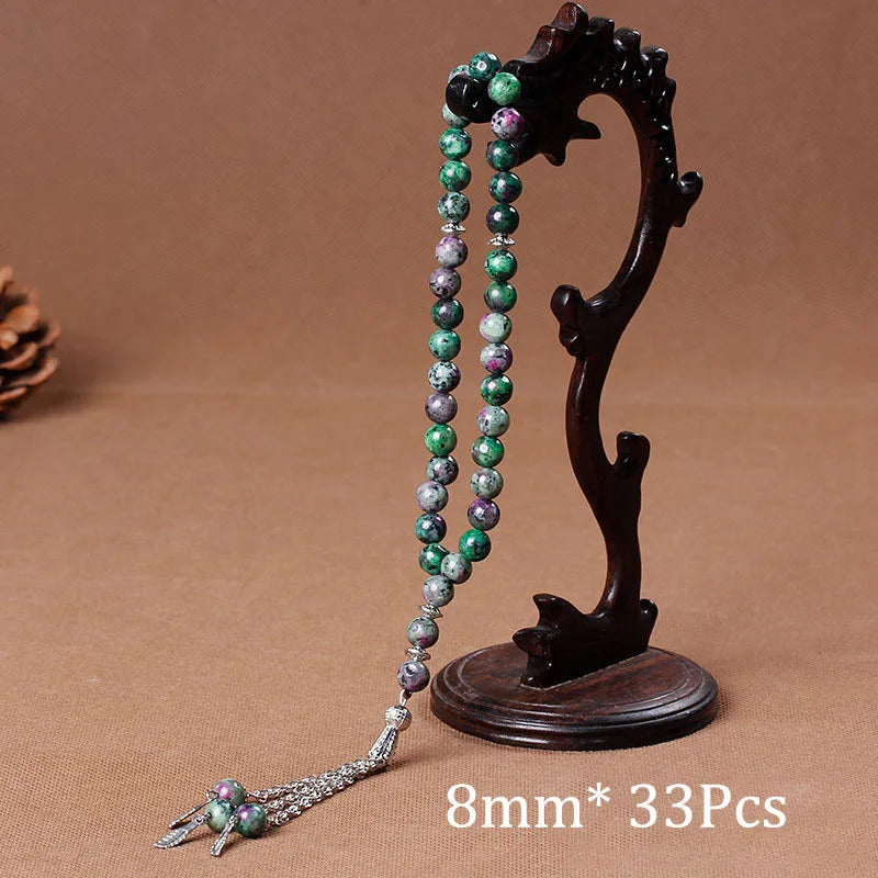 A dark wooden prayer bead necklace featuring green and purple agate beads and a tassel, displayed on a brown background.