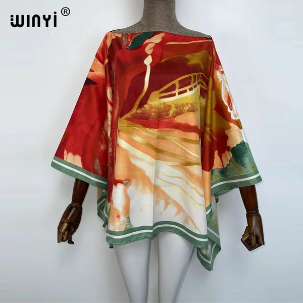 A woman is wearing a flowing, colorful batwing abaya top with abstract paint designs in shades of red, orange, and green.