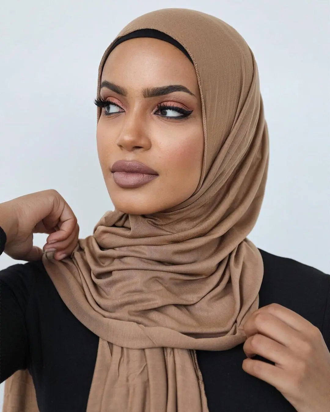 Une femme portant un foulard hijab en jersey beige et des vêtements noirs.