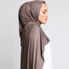 Eine Frau trägt einen braunen Baumwoll-Jersey-Hijabschal über Kopf und Schultern.