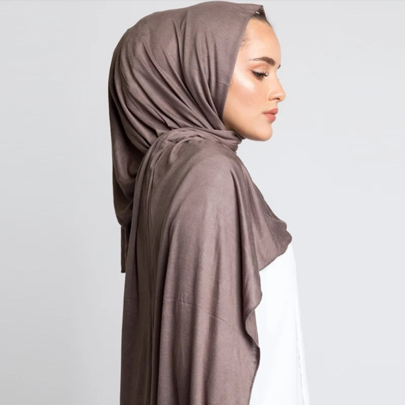 Eine Frau trägt einen braunen Baumwoll-Jersey-Hijabschal über Kopf und Schultern.