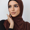Une femme portant un foulard hijab en jersey de coton brun uni, regardant légèrement de côté.