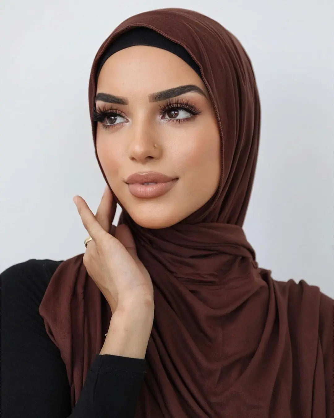 Une femme portant un foulard hijab en jersey de coton brun uni, regardant légèrement de côté.
