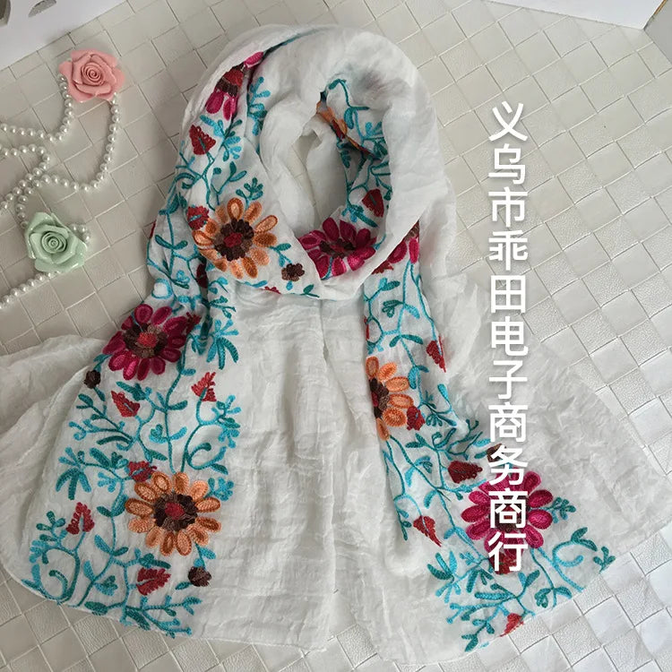 Weißer Stoff mit floraler Stickerei in rosa, orange und blau auf einem Schal oder Tuch.