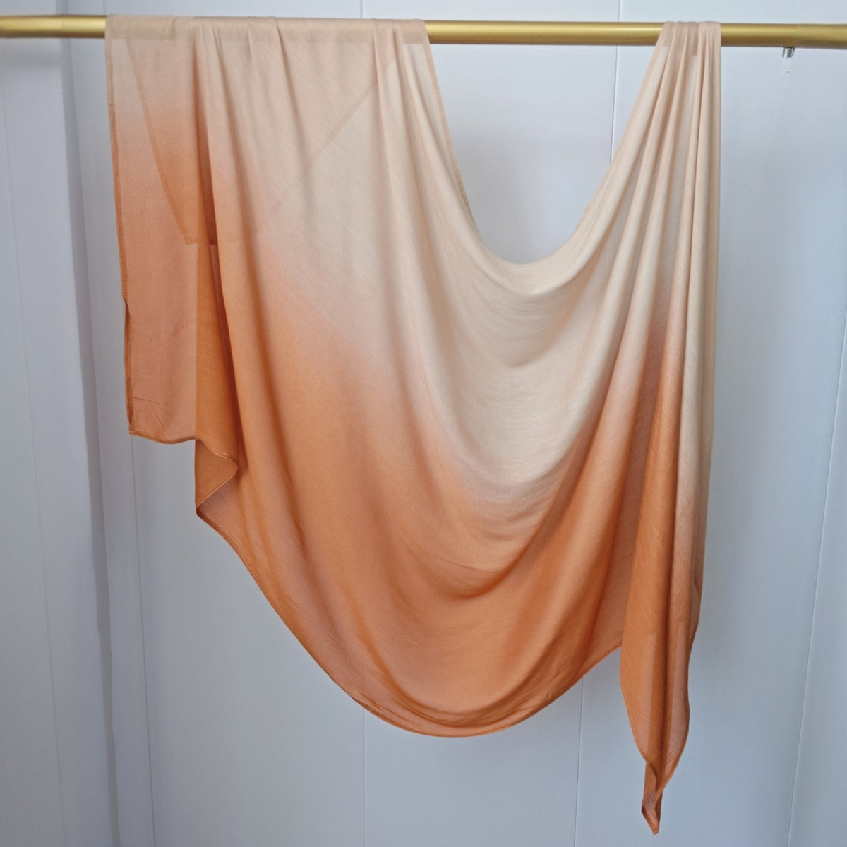 Pañuelo de hijab de algodón rayón con degradado ombré en color melocotón o terracota colgado en una percha.
