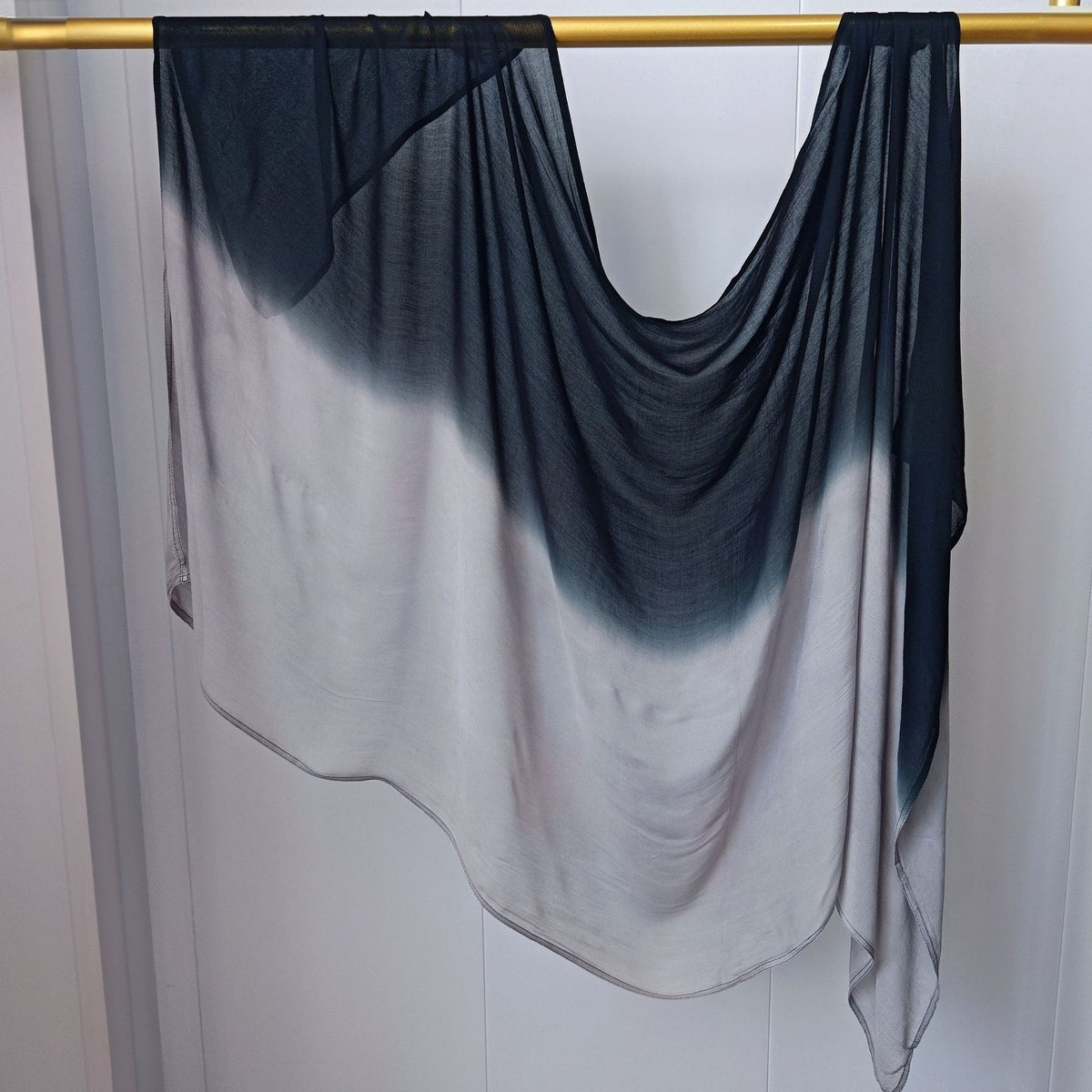 Pañuelo de hijab de algodón rayón en degradado azul oscuro y blanco colgando en una varilla de madera.
