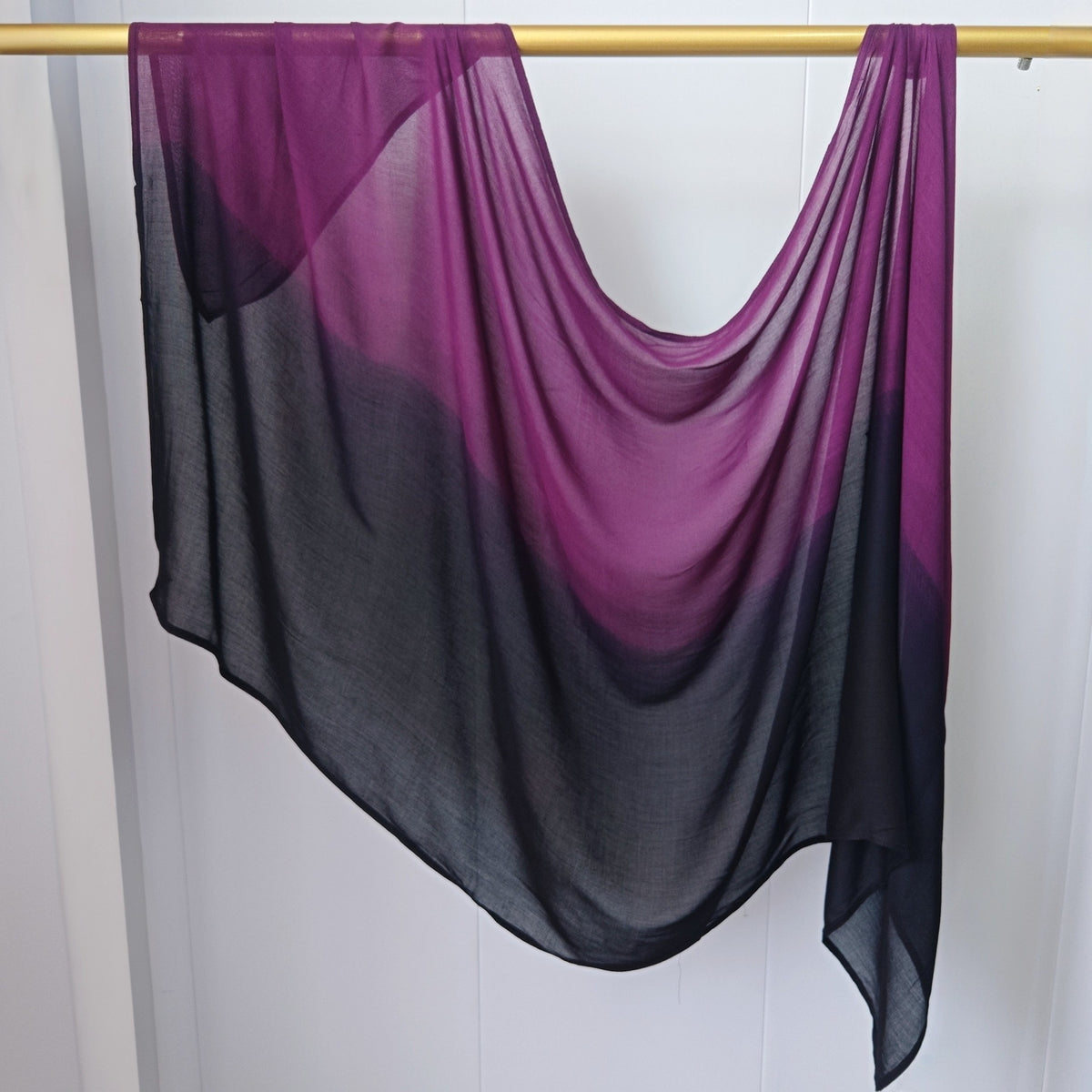 Pañuelo de hijab en degradado morado y negro transparente de algodón rayón colgado en una barra de madera.