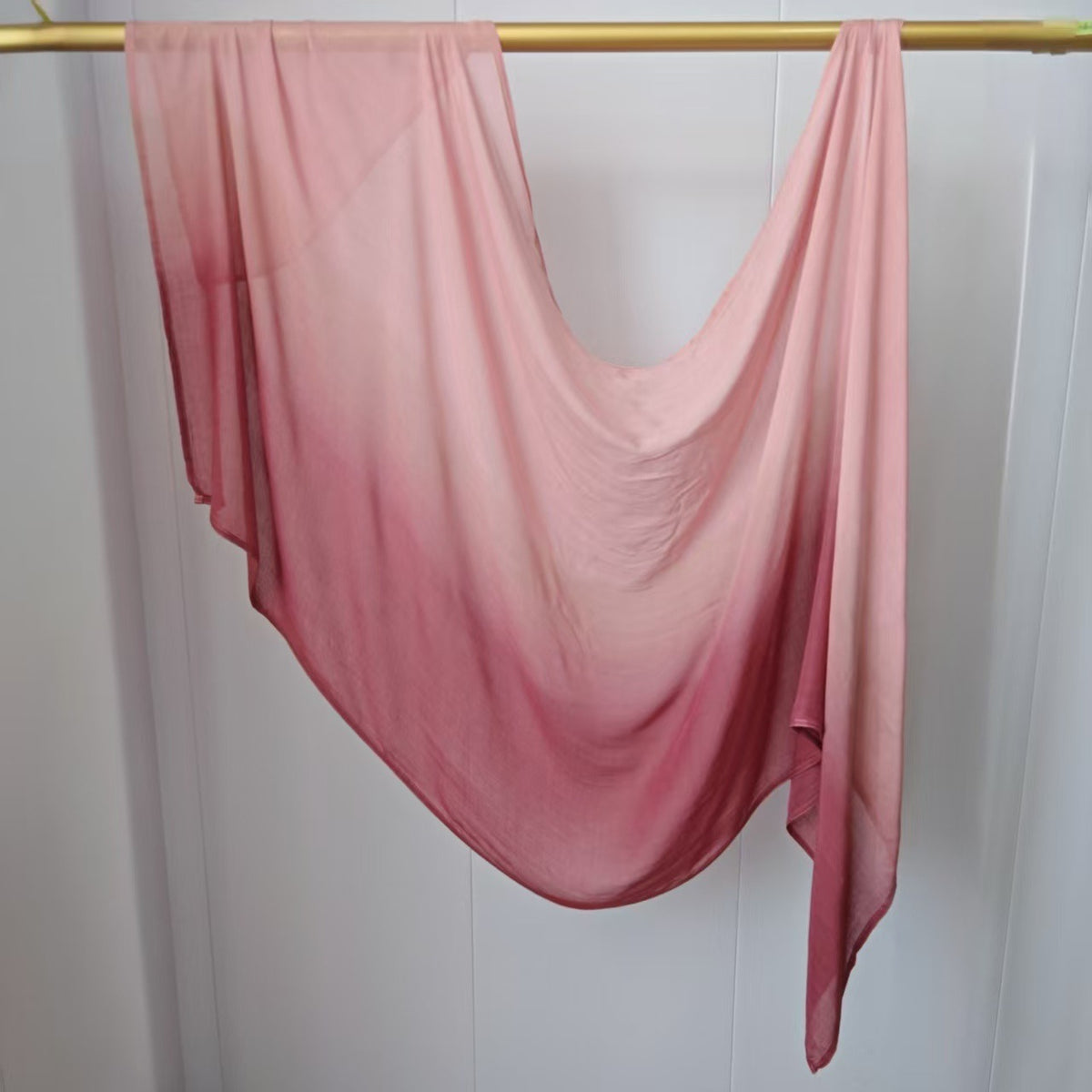 Pañuelo hijab de algodón rayón en degradado rosa transparente colgado en una varilla de madera.