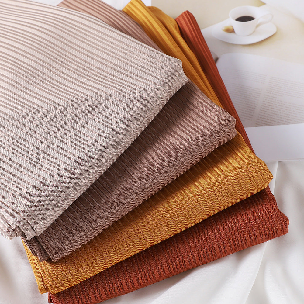 Una pila de pañuelos de hijab de jersey de algodón en varios tonos tierra, incluyendo beige, marrón y naranja.