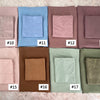 A collection of eighteen folded soft modal rayon hijab sets in various muted earth tones and blues.