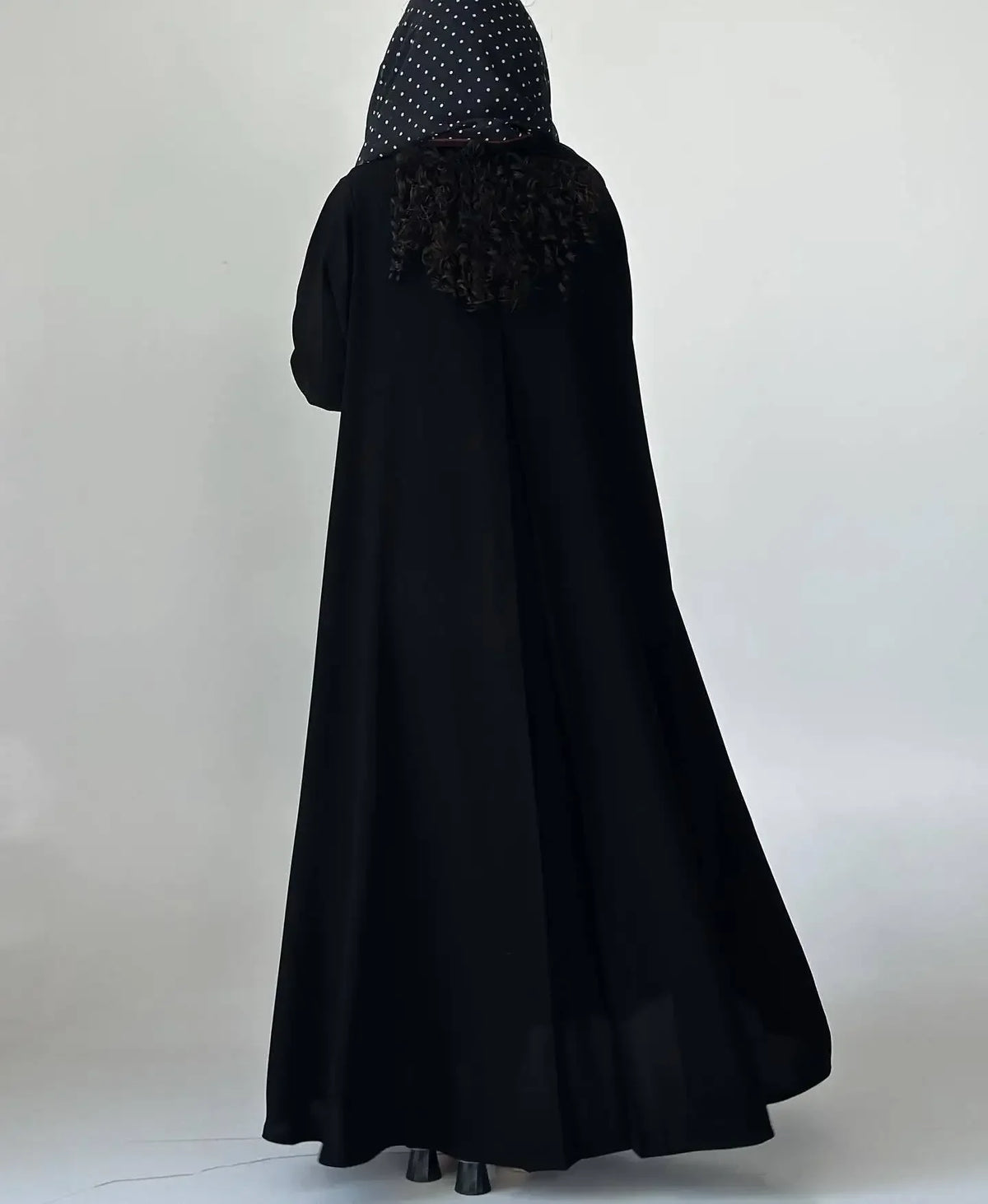 Langes schwarzes Abaya-Kleid mit dunklem, gemustertem Hijab und durchscheinender Überlappung.
