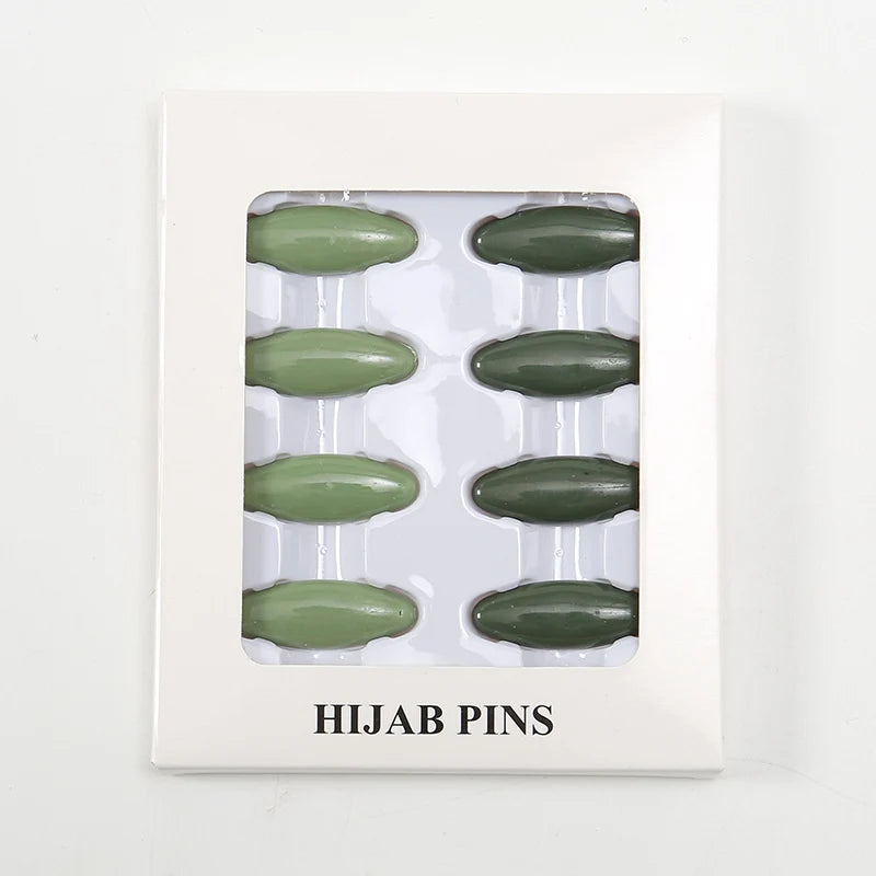 Un juego de ocho pines para hijab verde olivo exhibidos en un soporte de plástico blanco.
