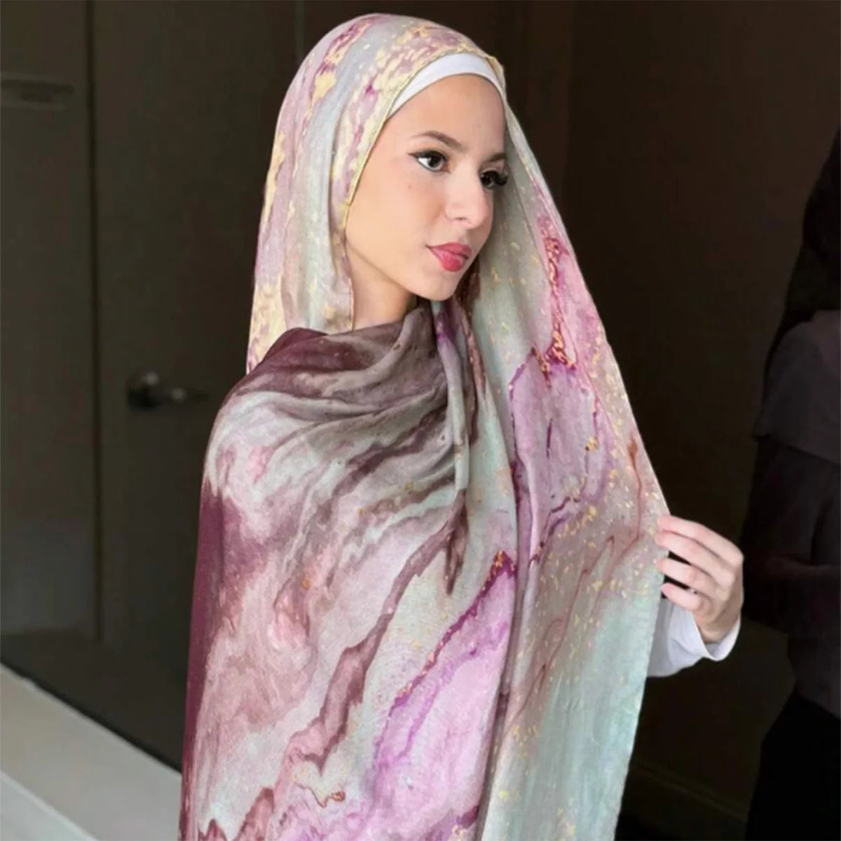 Eine Frau trägt einen fließenden Leinen-Baumwoll-Islamischen Schal mit Aquarellmuster in Rosa-, Violett- und Grüntönen.