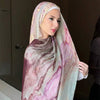 Eine Frau trägt einen Leinen-Baustoff-Hijab-Schal mit Aquarelldruck in Rosa-, Violett- und Grüntönen.