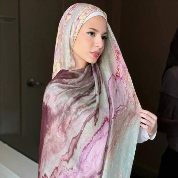 A woman wearing a watercolor print linen cotton hijab scarf in shades of pink, purple, and green.