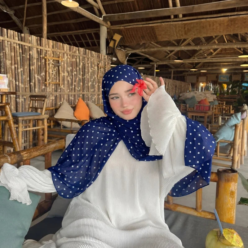 Eine Frau mit weißem Oberteil und blau-polka-dotiertem Hijab sitzt in einem rustikalen Holzinterior.