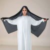 Eine Frau trägt ein weißes langes Kleid und einen schwarzen Instant-Hijab mit Riemchen, über ihren Kopf drapiert.