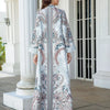 Femme portant une élégante abaya en perles de diamant à motifs floraux dans un cadre architectural blanc.
