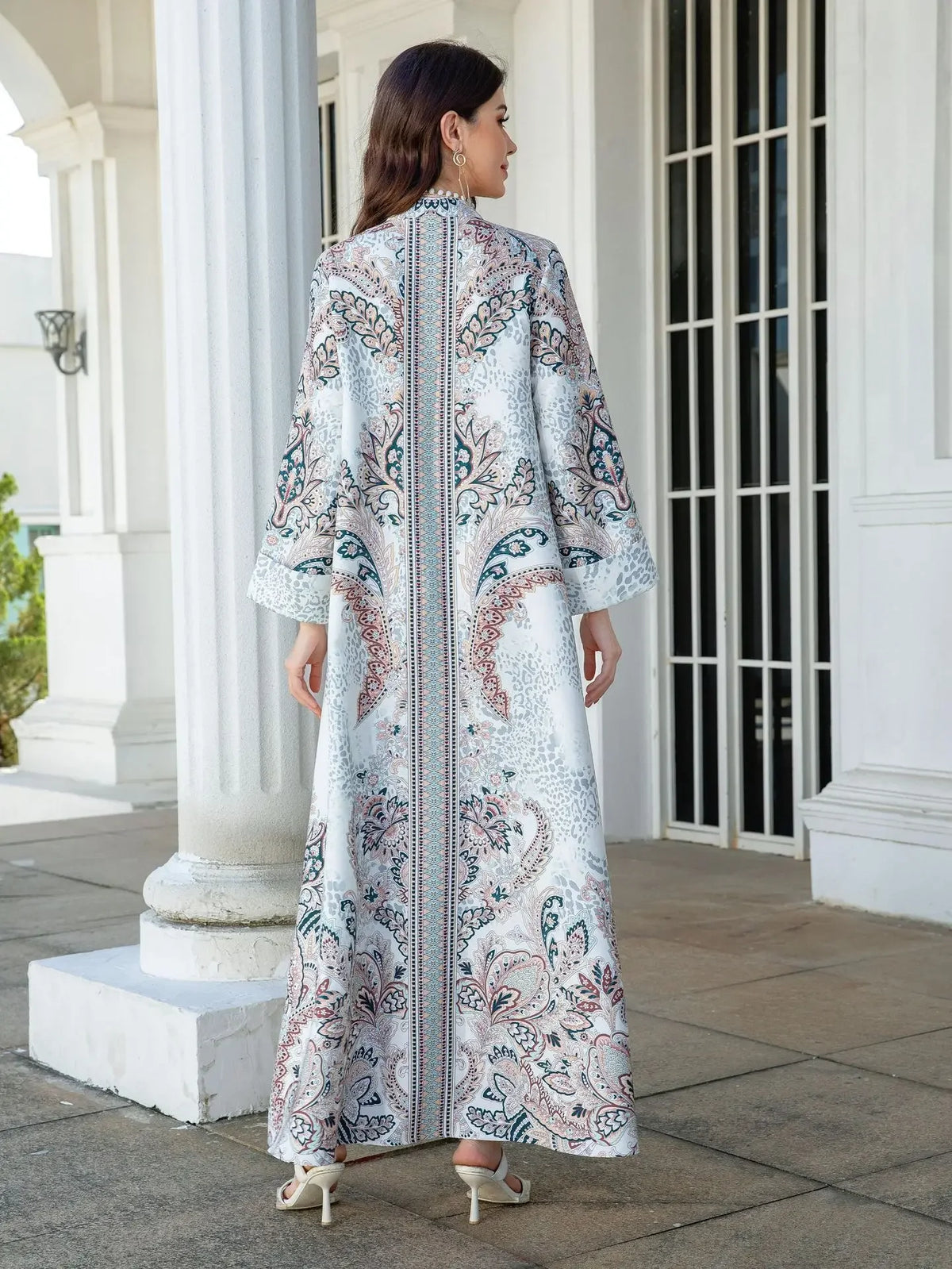Femme portant une élégante abaya en perles de diamant à motifs floraux dans un cadre architectural blanc.