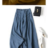 Nahaufnahme von beige-blauen Leinen-Palazzo-Hosen mit weitem Bein, kombiniert mit einer schwarzen Clutch und weißen Schnürsch