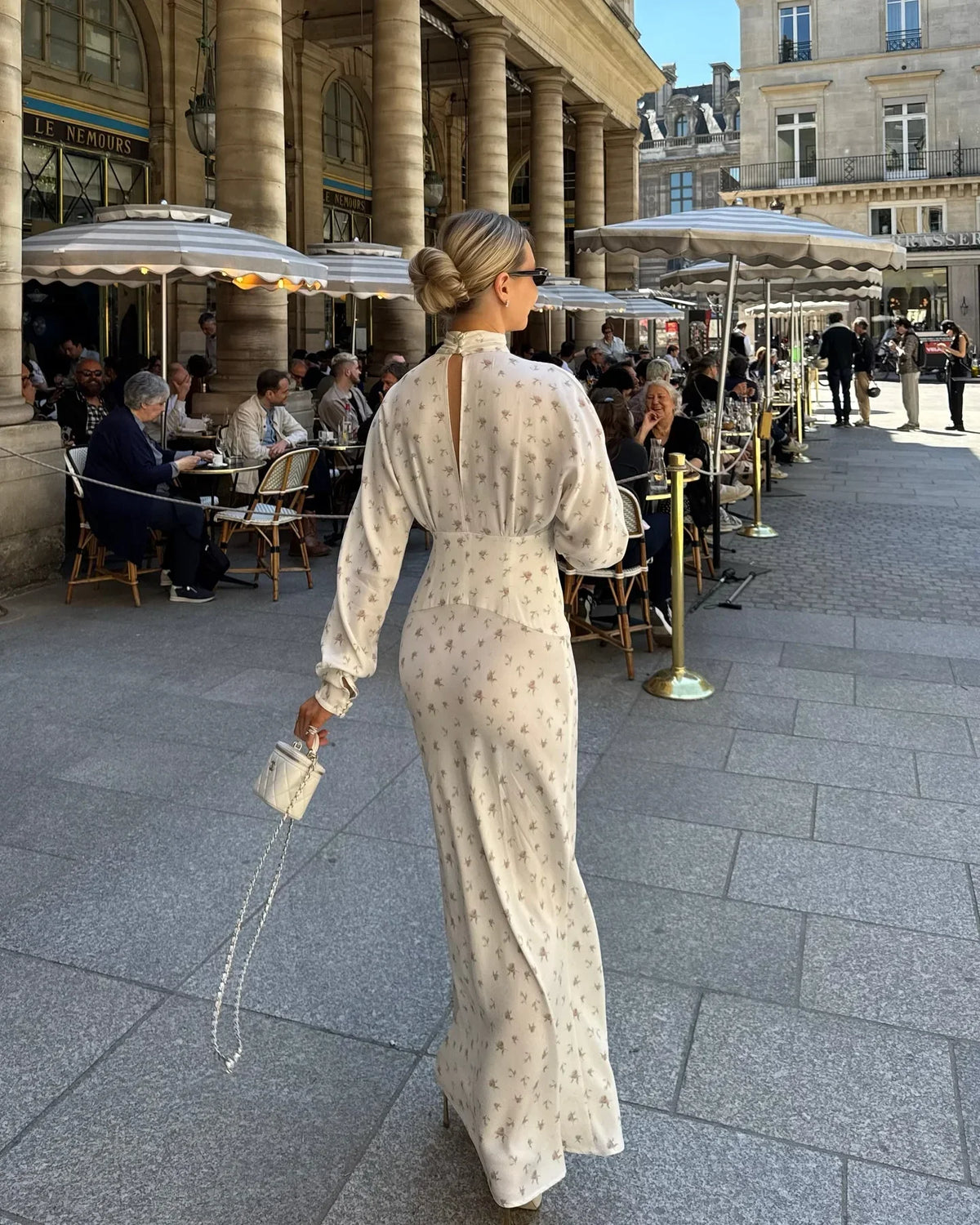 Una mujer con un vestido largo de satén estampado floral camina al aire libre en un mercado histórico.