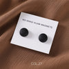 White magnetic board with two black round magnets for hijab clips placed on a brown fabric.
