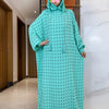 Una mujer vistiendo un abaya de algodón color verde azulado con capucha y lunares negros de polka, parada en un pasillo.