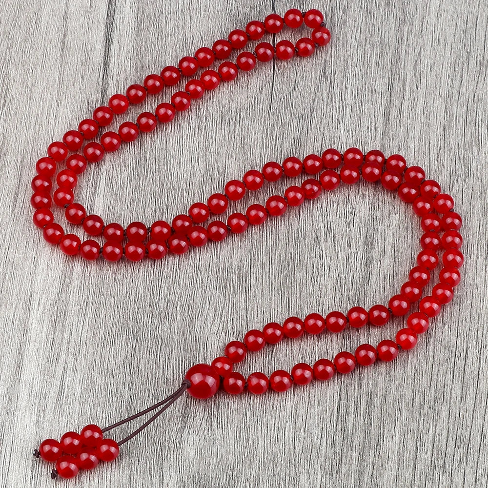 Eine Reihe roher, roter Natursteinchenperlen, drapiert auf einer grauen Holzoberfläche.