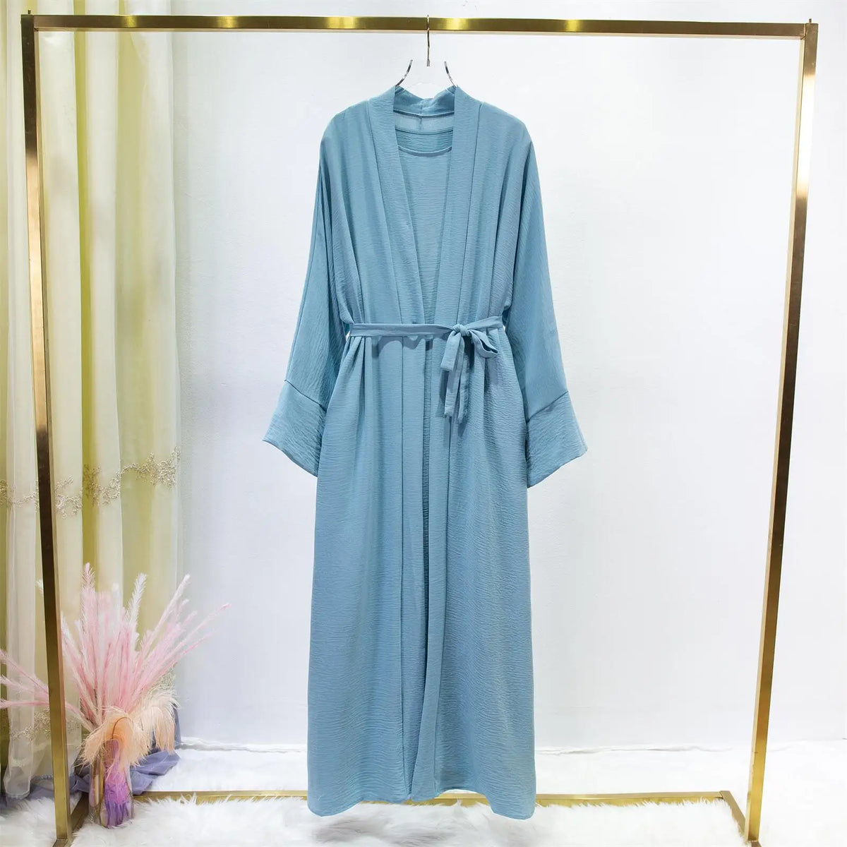 Un conjunto de jilbab de dos piezas azul claro para mujer, exhibido en percha sobre fondo blanco.
