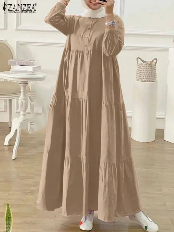 A woman models a long, beige Muslim abaya kaftan dress with long sleeves and a high neckline.