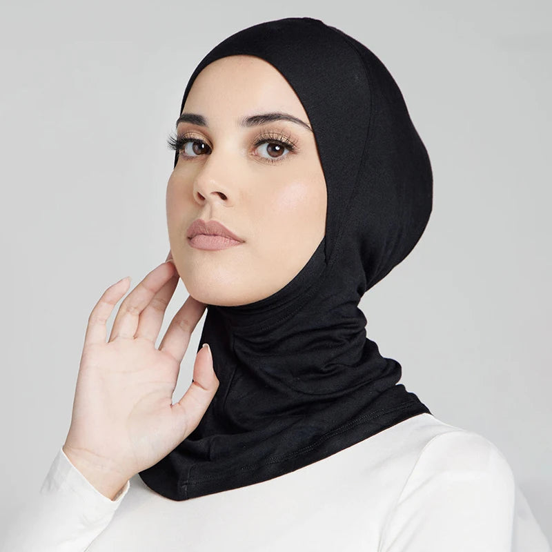 Eine Frau trägt einen schwarzen, dehnbaren Baumwoll-Hijab-Bonnet und blickt direkt in die Kamera.