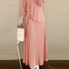 Une femme portant une robe et un haut plissés roses avec des boutons dorés, stylisés comme un élégant ensemble musulman.