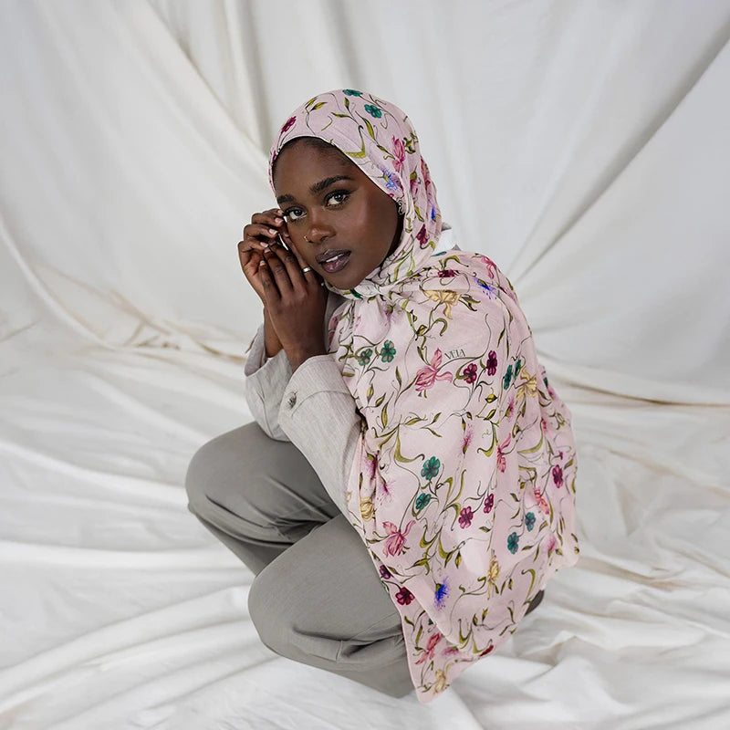A woman wearing a watercolor printed pink scarf hijab, looking directly at the camera.