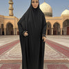 Une femme portant une caftan abaya noire et fluide se tient dans une cour avec une architecture historique.