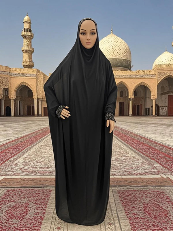 A woman wearing a black flowy kaftan abaya dress stands in a large courtyard with historical architecture.