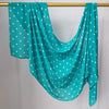 Una bufanda transparente color verde azulado con lunares blancos colgada en un perchero dorado.